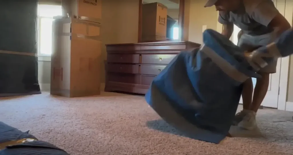 Mover pulling a blue cover over furniture in a bedroom