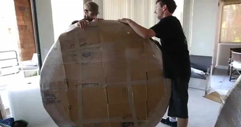 Two movers lifting a round tabletop wrapped in cardboard